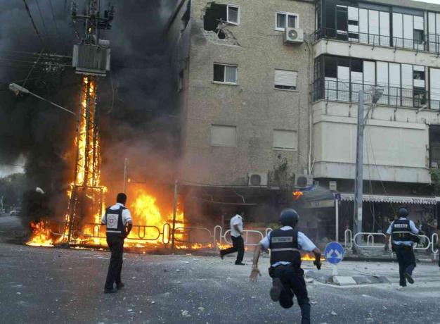 Az izraeli rendőrök az égő villanyoszlop és a megrongálódott építési pillanatok helyszínére sietnek, miután a Hezbollah rakéták zöreje 2006. július 13-án az izraeli Nahariya északi városában elütött.