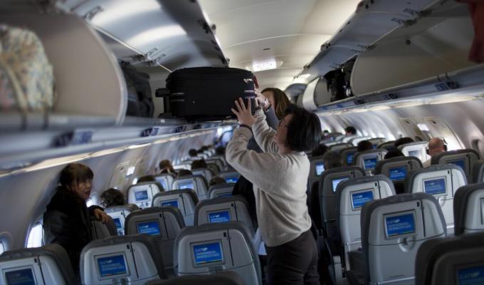 Mujer colocando maleta en compartimento superior de avión.