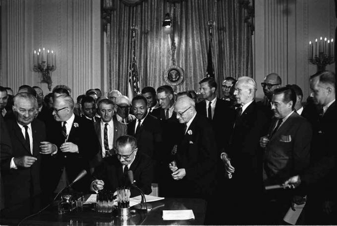 Lyndon B. elnök Johnson aláírja az 1964-es polgári jogi törvényt, amikor Martin Luther King, Jr. és mások figyelnek.